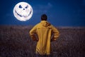 Man standing in a wheat field back to the camera in a night and watching scary  moon face  in sky Royalty Free Stock Photo