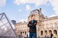 A young man stands against the background of the Louvre building.Paris