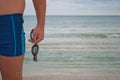 Young man stands against the sea shore beach sand waves water horizon holds in his hand sunglasses for swimming Royalty Free Stock Photo