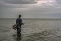 Young man stands alone in waders in the shallow waters fishing with a casting rod