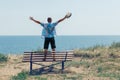 A young man stands on a bench with his arms raised and enjoys the view of the sea Royalty Free Stock Photo