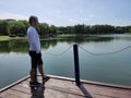 The young man stands on bridge and meditates in the forest on the shore of the lake. Summer sunny day. Royalty Free Stock Photo