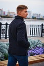 A young man stands on the embankment of the city of Blagoveshchensk. Short haircut. Black jacket and jeans. Flower bed