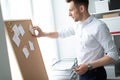 A young man stands near a board with stickers and holds a pen in his hand. A young man tears off a sticker. Royalty Free Stock Photo