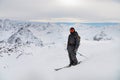 young man stands on a rock at the top of a mountain with a backpack and skis, watching a long alpine panorama Royalty Free Stock Photo