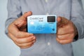 Young man stands at white background and holds credit card with fingerprint sensor in one hand and points with index finger of