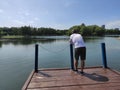 The young man stands on bridge and meditates in the forest on the shore of the lake. Summer sunny day. Royalty Free Stock Photo