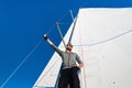 Young man stands on yacht boom and looks forward. He holds on mast rope with hand. Young man poses. He wears grey hoody