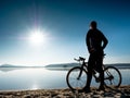 Young man staying on the shore of the lake with bicycle at sunset Royalty Free Stock Photo