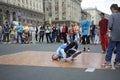 Young man, street dancer, performimg break dance on the pavement, blurred people watching on a background