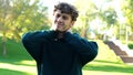 Young Caucasian man stretching before outdoor activities. Guy feeling pain in his neck standing in green park on sunny Royalty Free Stock Photo