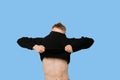 Young man struggling to pull down t-shirt over blue background