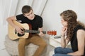 Young man strumming guitar besides female friend