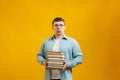 Young man student in glasses holds stack of university books from college library on yellow background. Happy guy smiles, he is Royalty Free Stock Photo