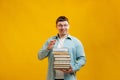 Young man student in glasses holds stack of university books from college library on yellow background. Happy guy smiles, he is Royalty Free Stock Photo