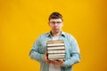 Young man student in glasses holds stack of university books from college library on yellow background. Happy guy smiles, he is Royalty Free Stock Photo