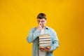 Young man student in glasses holds stack of university books from college library on yellow background. Happy guy smiles, he is Royalty Free Stock Photo