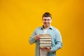 Young man student in glasses holds stack of university books from college library on yellow background. Happy guy smiles, he is Royalty Free Stock Photo