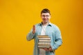 Young man student in glasses holds stack of university books from college library on yellow background. Happy guy smiles, he is Royalty Free Stock Photo