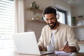 Young man student with laptop and headphones indoors at home, studying.