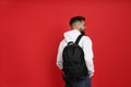 Young man with stylish backpack on red background, back view. Space for text