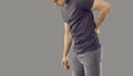 Young man suffering from back pain due to large physical exertion isolated on gray background.