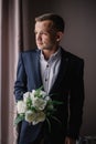 Young man in a suit with a bouquet looks out the window Royalty Free Stock Photo
