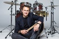 Young handsome man in suit sitting in front of drum set isolated on white background Royalty Free Stock Photo