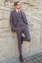 Young man with a suit and tie is waiting for a person near a stone wall