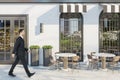 Man in suit walking past creative concrete cafe exterior with terrace furniture in daylight