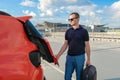 A young man with a suitcase in his hands is stacking in the trunk of a car in the parking lot of the airport outdoors. Royalty Free Stock Photo