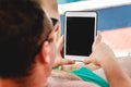 A young man in sunglasses holds a tablet in his hands. Freelancer job concept on the beach and vacation Royalty Free Stock Photo