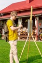 Young man paints painting outside his country house holding palette of paints Royalty Free Stock Photo