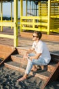 Young man in sunglasses sitting on the steps of a wooden building on the beach Royalty Free Stock Photo