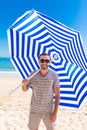 Young man in sunglasses walking on the beach with sun solar umbrella on sea resort. Summer vocation Royalty Free Stock Photo