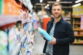 Young man in the supermarket in the household chemicals department. Large selection of products. A brunette in a glasses Royalty Free Stock Photo