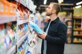 Young man in the supermarket in the household chemicals department. Large selection of products. A brunette in a glasses Royalty Free Stock Photo