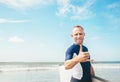 Young man Surfer portrait showing surfer`s famous Shaka sign gesture in camera when he comming with long surf board to waves.