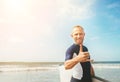 Young man Surfer portrait showing surfer`s famous Shaka sign gesture in camera when he comming with long surf board to waves.