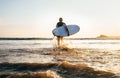 Young man Surfer taking surfboard and comming with long surf board to waves on the evening sunset sky background. Active holidays