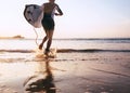 Young man Surfer taking surfboard and running with long surf board to waves on the evening sunset sky background. Active holidays Royalty Free Stock Photo