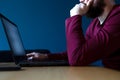 Young man surfs the internet on his laptop late at night with blue background, working late with moody colors blue and red Royalty Free Stock Photo