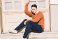 young man in sweater sitting on steps in front of house and posing Royalty Free Stock Photo