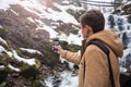 A young man takes a picture of a waterfall on a mobile phone in Royalty Free Stock Photo