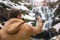 A young man takes a picture of a waterfall on a mobile phone in Royalty Free Stock Photo