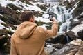 A young man takes a picture of a waterfall on a mobile phone in Royalty Free Stock Photo