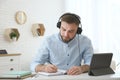 Young man taking notes during online webinar at table indoors Royalty Free Stock Photo