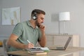 Young man taking notes during online webinar at table indoors Royalty Free Stock Photo