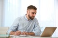 Young man taking notes during online webinar at table