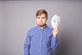 Young man taking off plain white mask revealing face, gray background Royalty Free Stock Photo